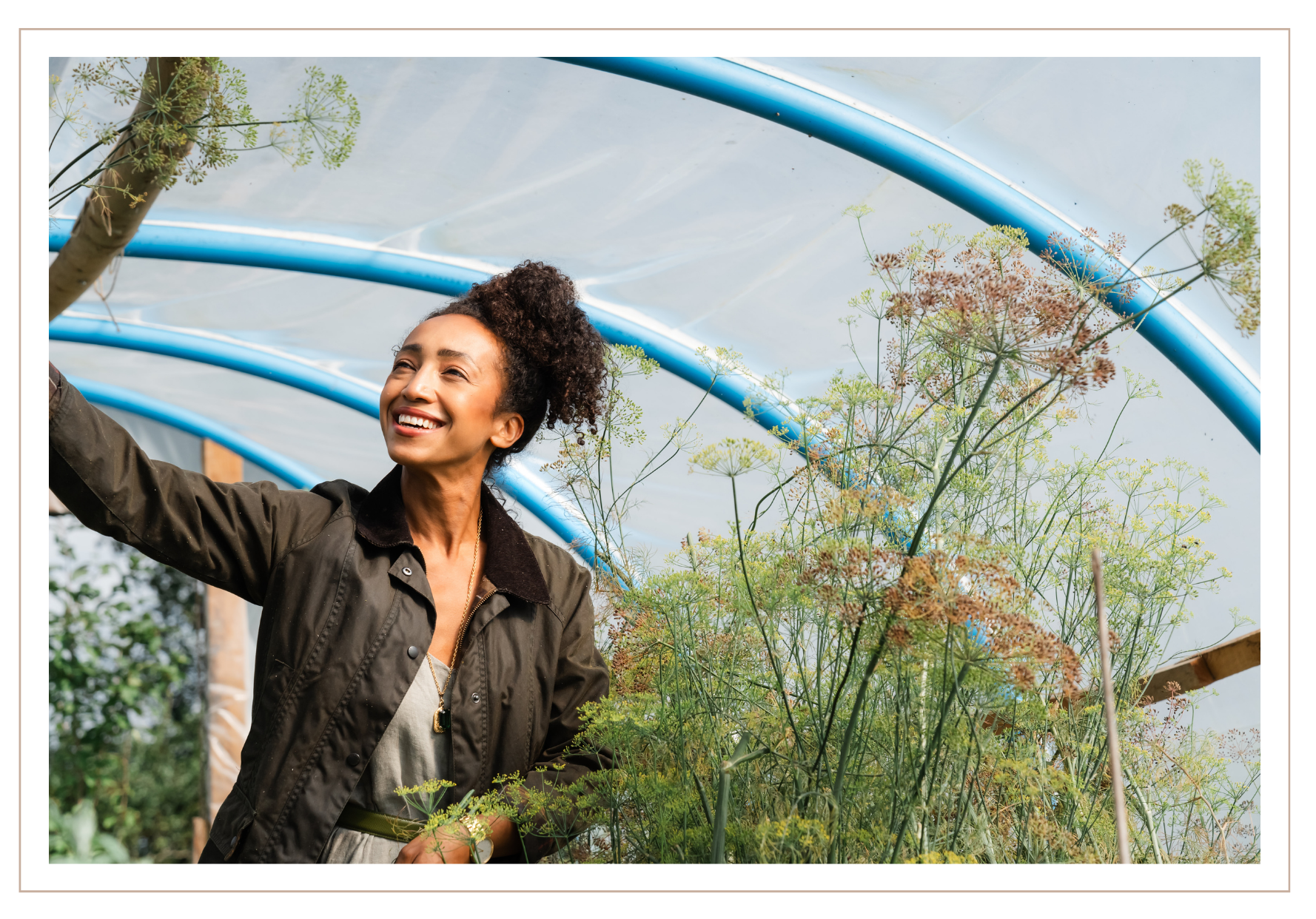 Hazel Gardiner stands in a. poly tunnel with  greenery around her, wearing a dark jacket over a light top.